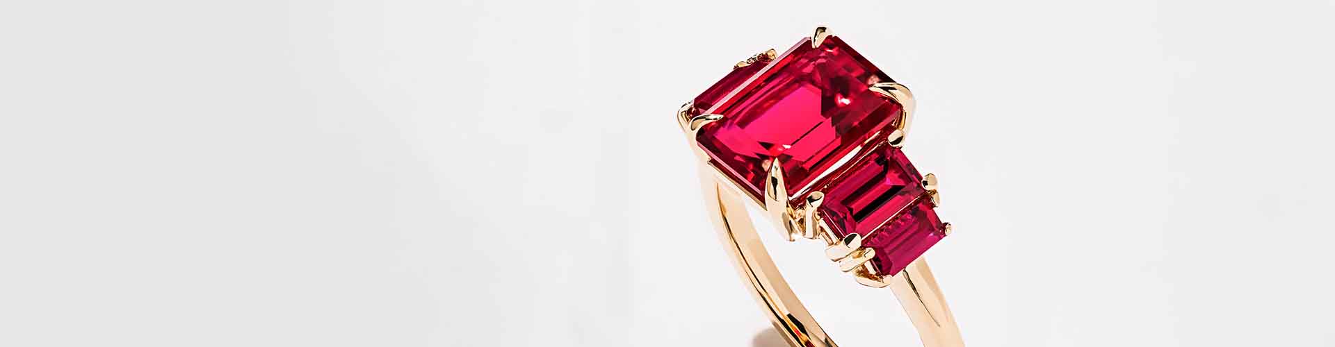 Image of a stunning MiaDonna custom five-stone ruby ring featuring a claw-pronged, large emerald-cut ruby center stone flanked by progressively smaller emerald-cut rubies with round prongs, and a rose gold band.