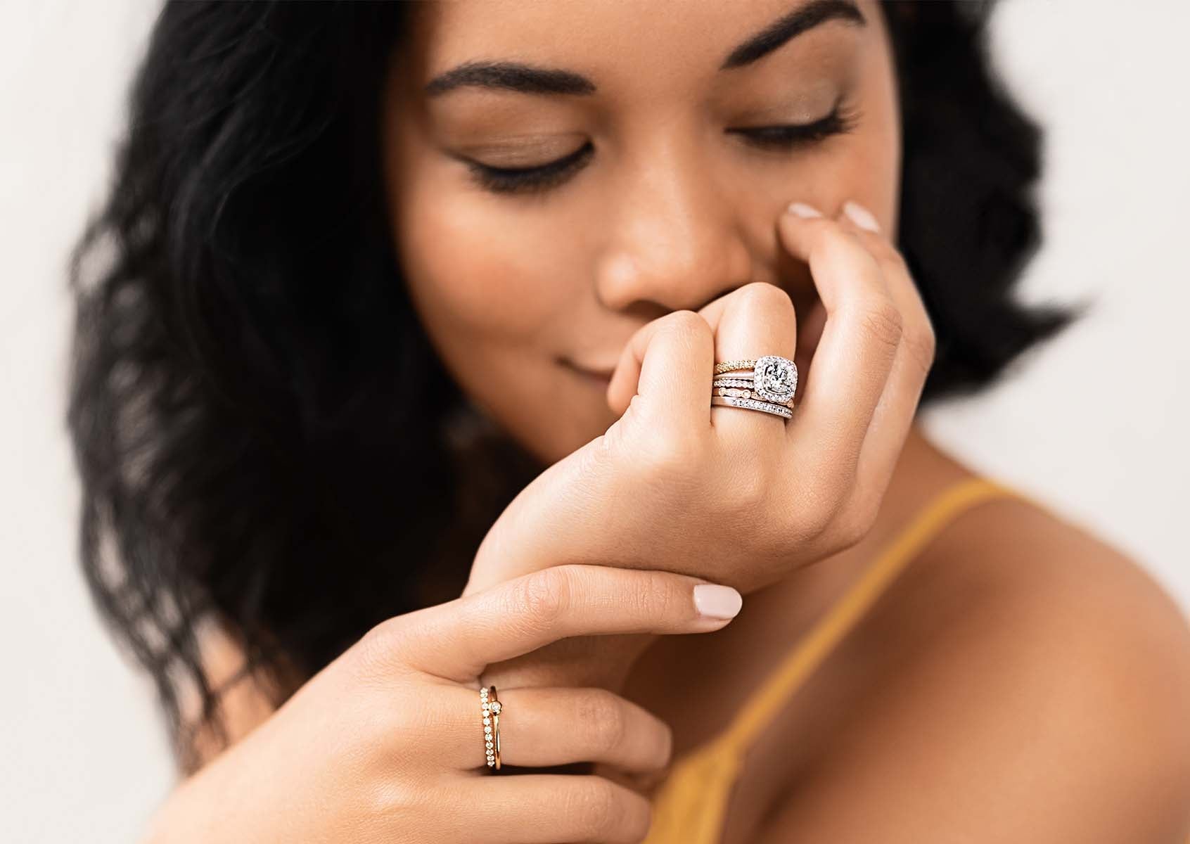 A model smiles softly while display a stack of MiaDonna fashion rings featuring white gold and conflict free, lab-created diamonds.
