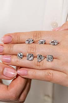 A woman demonstrates the look of various shapes and sizes of MiaDonna loose lab created diamonds by showing them lined along the fingers atop her closed hand. 