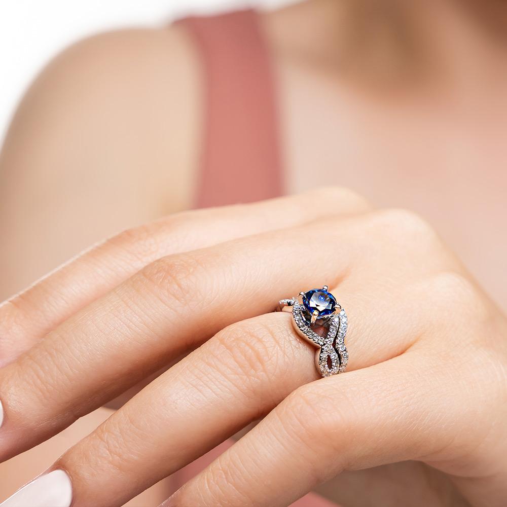 Shown with a 1.0ct Round cut Blue Sapphire Lab-Created Gemstone with infinity style diamond accented band with matching wedding band 