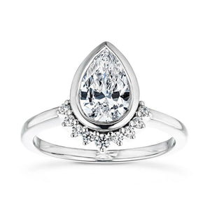 Unique modern bezel set engagement ring with tear drop diamond center stone surrounded by half halo of diamonds set in 14k white gold