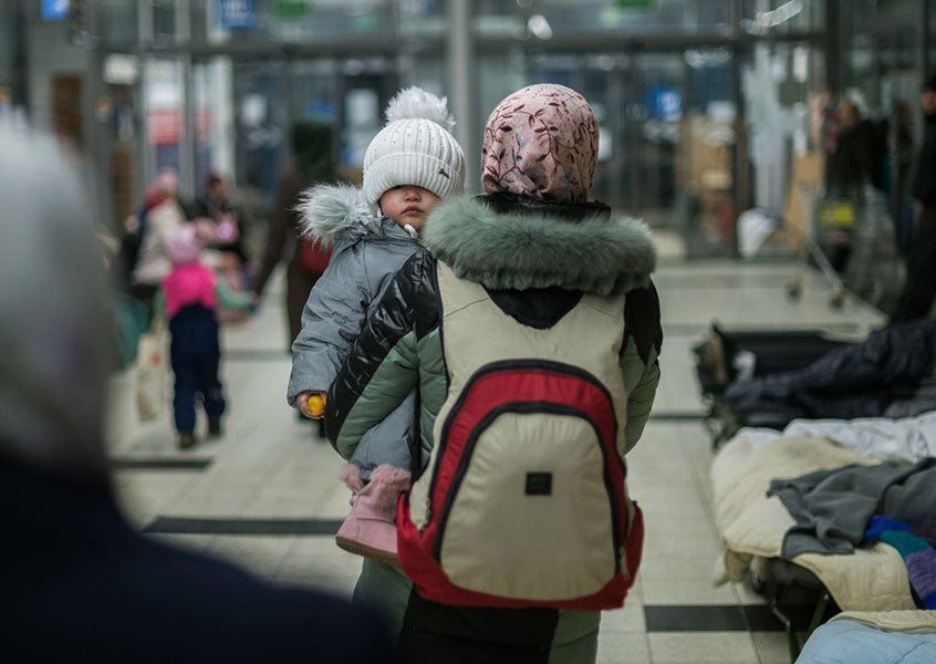 At a Ukrainian refugee relief center in Poland donated to by The Greener Diamond, a winter-clad Ukrainian woman walks away holding a child facing the camera