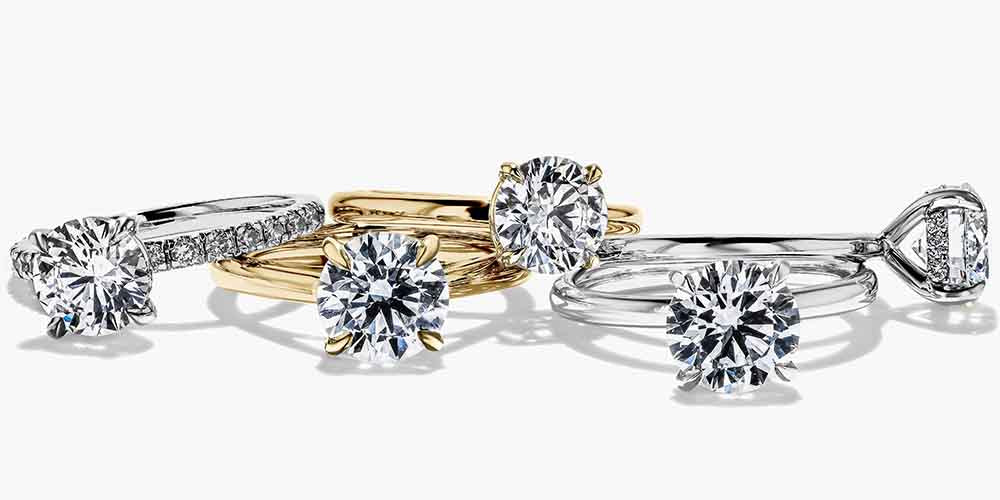 A collection of MiaDonna engagement rings in various colors, including gold, silver, rose gold, and platinum, each featuring a round cut lab created diamond center stone.