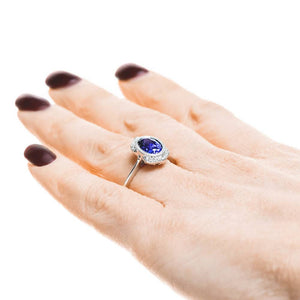 Ethical vintage style engagement ring with diamond halo and bezel set 2ct oval cut lab created blue sapphire in 14k white gold worn on hand sideview