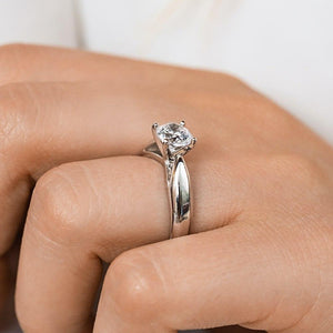 Modern solitaire engagement ring with wide band and cathedral style design featuring 1ct round cut lab grown diamond in platinum worn on hand
