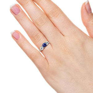 Three stone engagement with round cut lab grown diamonds and lab created blue sapphire center stone in 14k white gold worn on hand