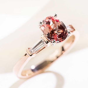 Three stone engagement ring with 1.5ct oval cut lab grown pink sapphire amid two baguette cut diamond side stones in 14k rose gold