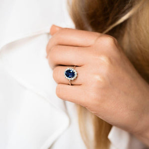Beautiful vintage style engagement ring with floral design halo around a 3ct lab created blue sapphire in 14k white gold worn on hand