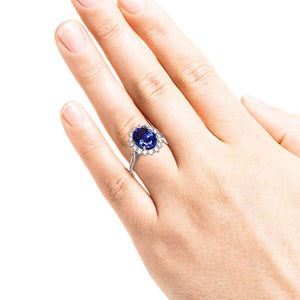 Vintage style engagement ring with floral design halo around a 3ct lab created blue sapphire in 14k white gold worn on hand