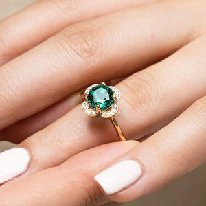 Nature inspired vintage style engagement ring with floral petal halo design around a 1ct round cut lab created emerald in 14k yellow gold
