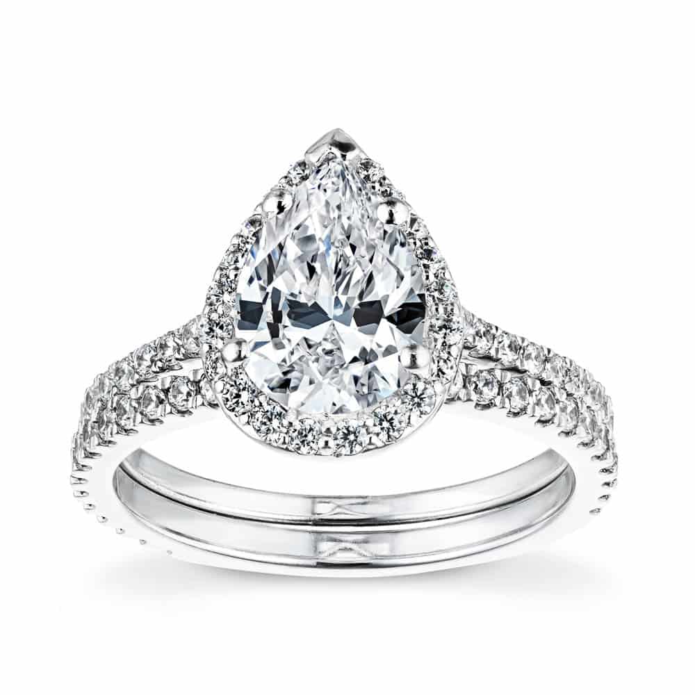 Shown with a 1.0ct Pear cut Lab-Grown Diamond with a diamond accented halo and band in recycled 14K white gold with matching wedding band