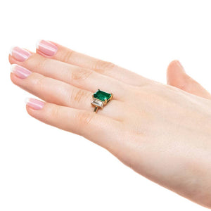 Three stone engagement ring with 2ct emerald cut lab created emerald center between baguette cut lab diamonds set in 14k yellow gold worn on hand sideview