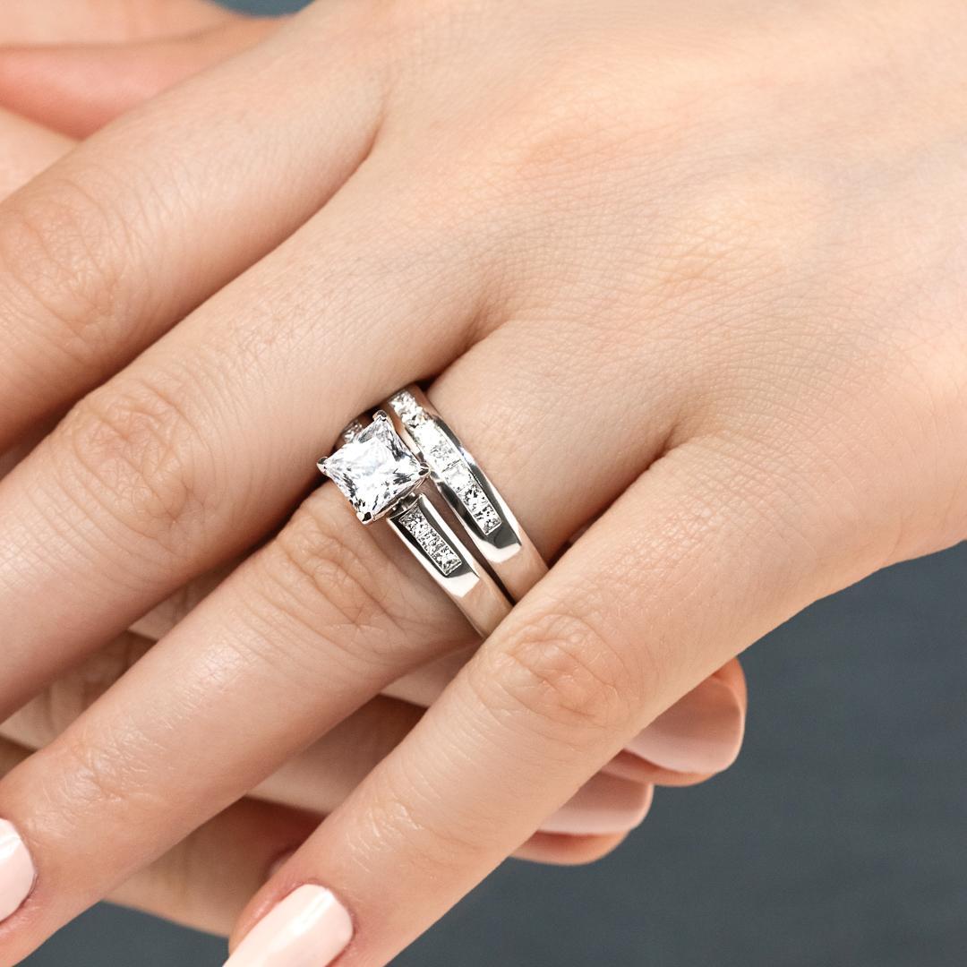 Melanie Wedding Set featuring a princess cut 1.50ct Diamond Hybrid® engagement ring in recycled 14K white gold with .30ctw side stones and a matching wedding band with .40ctw channel set stones 