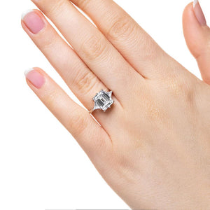 Three stone engagement ring with 2ct emerald cut lab grown diamond center stone with triangle side stones set in 14k white gold band worn on hand