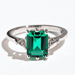 Stunning unique three stone engagement ring with 2ct emerald cut lab created emerald center stone with triangle diamond side stones set in 14k white gold band
