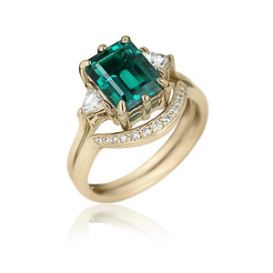 Emerald engagement ring with diamond side stones in 14k yellow gold setting with matching diamond accented wedding band