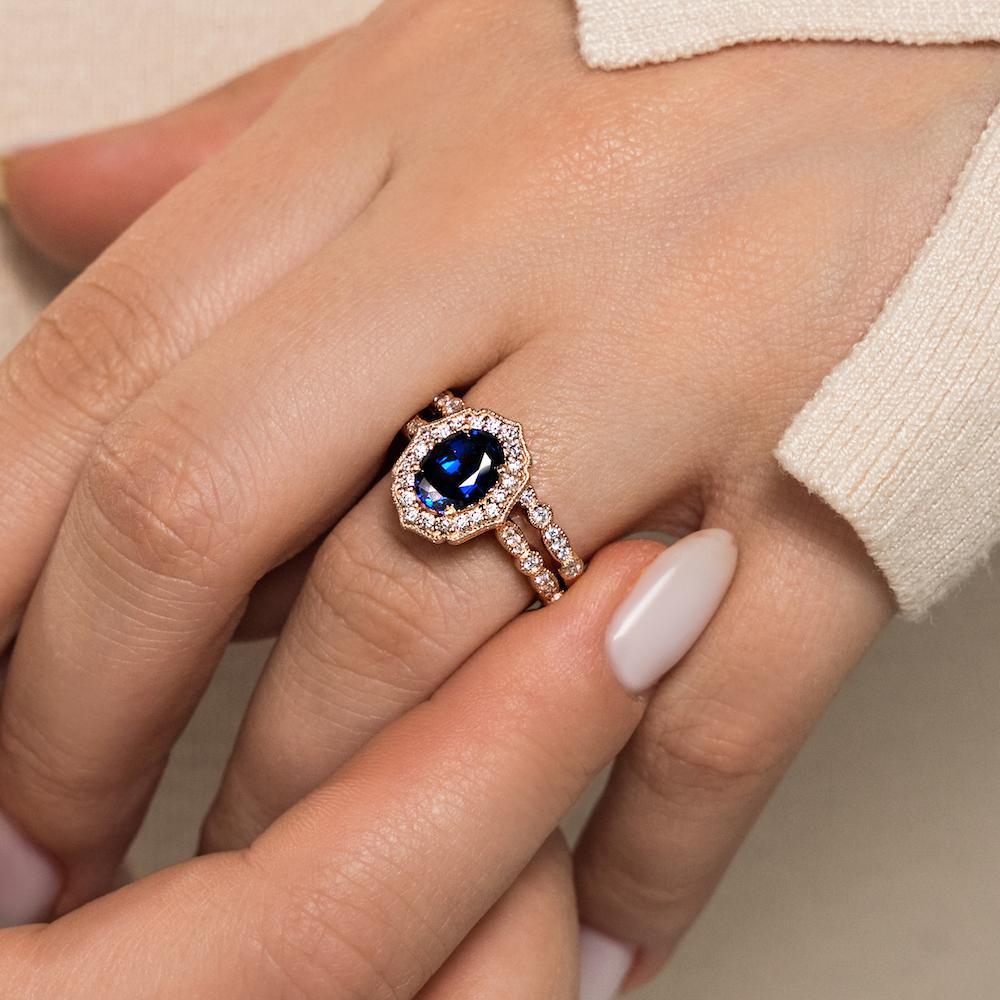 Shown with a 1.0ct Oval cut Blue Sapphire Lab-Created Gemstone with a diamond accented halo and filigree detailing in recycled 14K rose gold with matching wedding band, can be purchased together at a discounted price