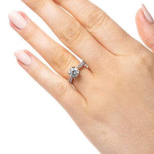 Vintage style nature inspired diamond accented engagement ring with a floral head holding a 1ct round cut lab grown diamond in 14k white gold band worn on hand