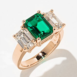 Stunning conflict free three stone engagement ring with 1ct emerald cut lab grown emerald center stone and two lab grown diamond side stones in 14k rose gold setting